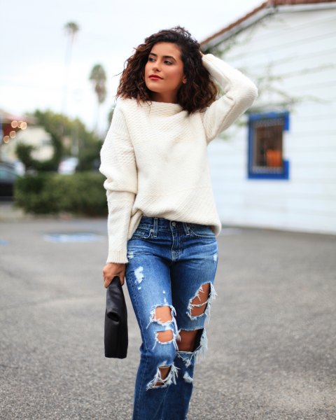 white, chunky sweater with torn jeans and clutch